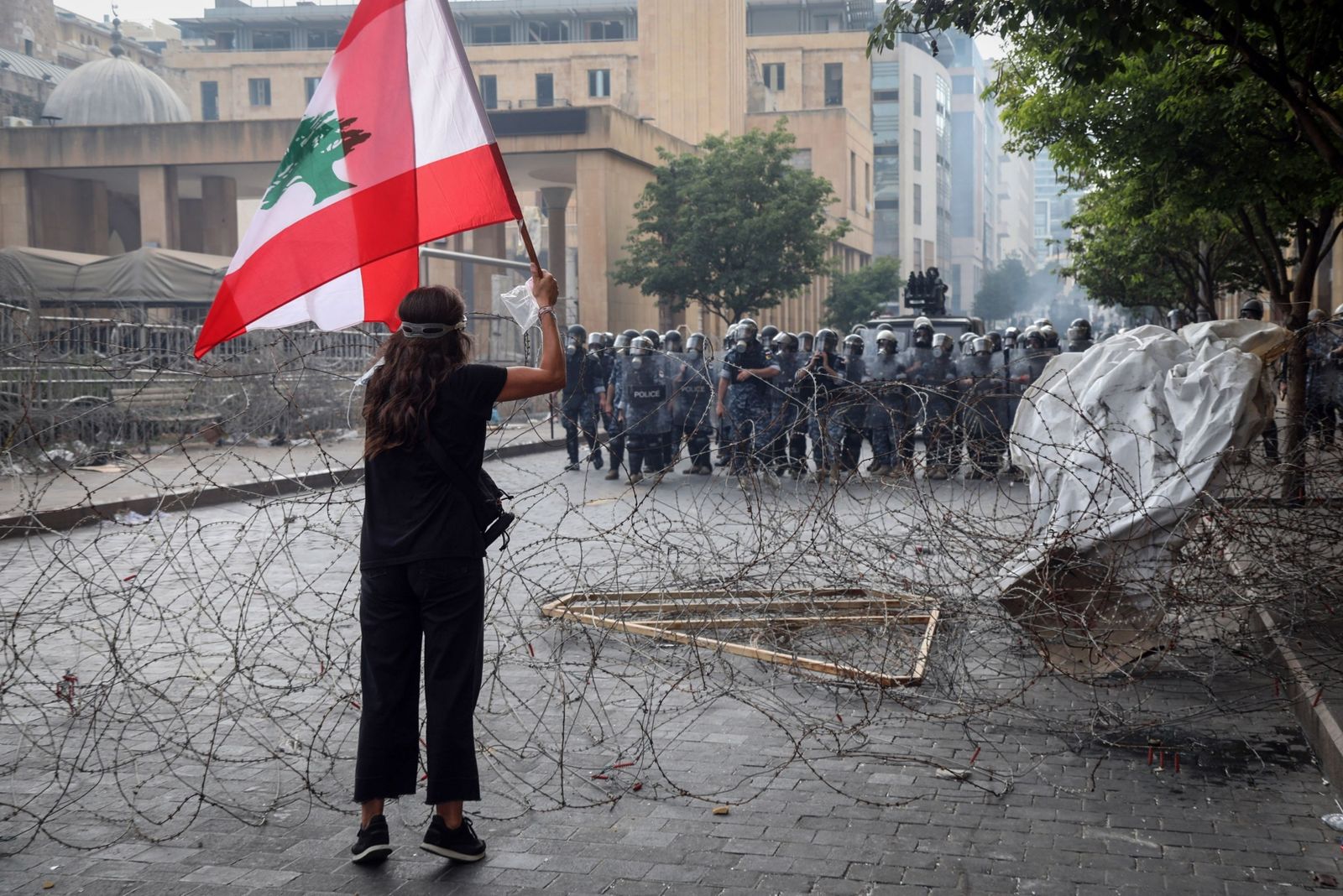 تلوّح بعلم لبناني أمام قوات أمن خلال نظاهرة قرب مقرّ البرلمان في بيروت - 8 أغسطس 2020 - Bloomberg