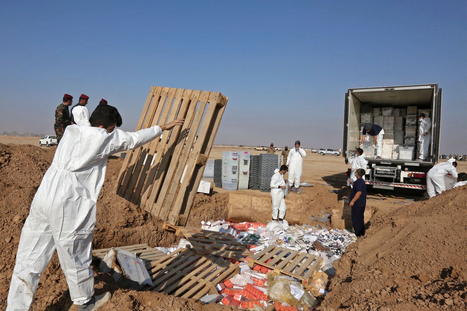 Iraqi government officials wearing white coveralls and face masks destroy nearly six tons of drugs, some of which had been in storage for more than a decade, in Baghdad's Nahrawan area on December 18, 2022. - Speaking in front of assembled media who were invited to cover the destruction near a military base outside Baghdad, he said it was the first 