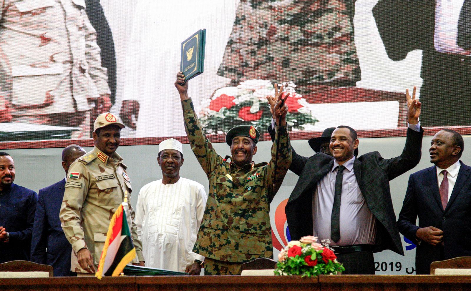 يومض زعيم الاحتجاج السوداني أحمد ربيع (الثاني إلى اليمين) بادرة النصر إلى جانب اللواء عبد الفتاح البرهان (وسط) ، رئيس المجلس العسكري الانتقالي الحاكم في السودان ، خلال احتفال حيث وقعوا على 