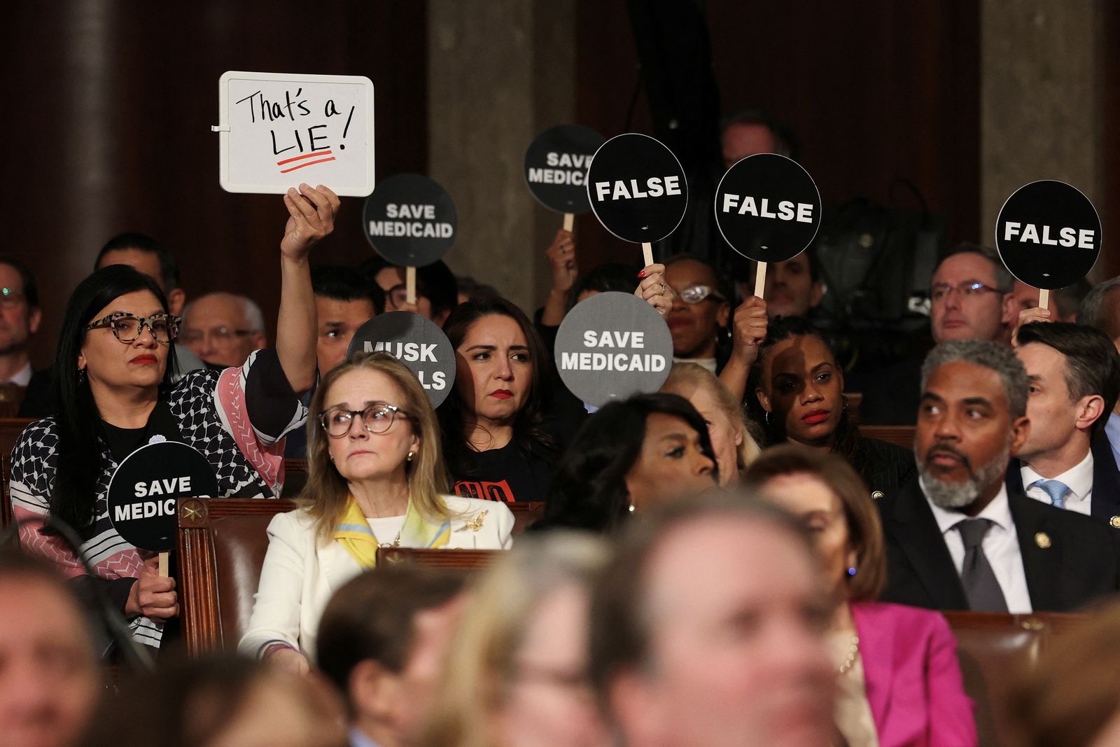 WASHINGTON, DC - MARCH 04: Democrats hold protest signs as U.S. President Donald Trump address a joint session of Congress at the U.S. Capitol on March 04, 2025 in Washington, DC.      Win McNamee/Pool via REUTERS