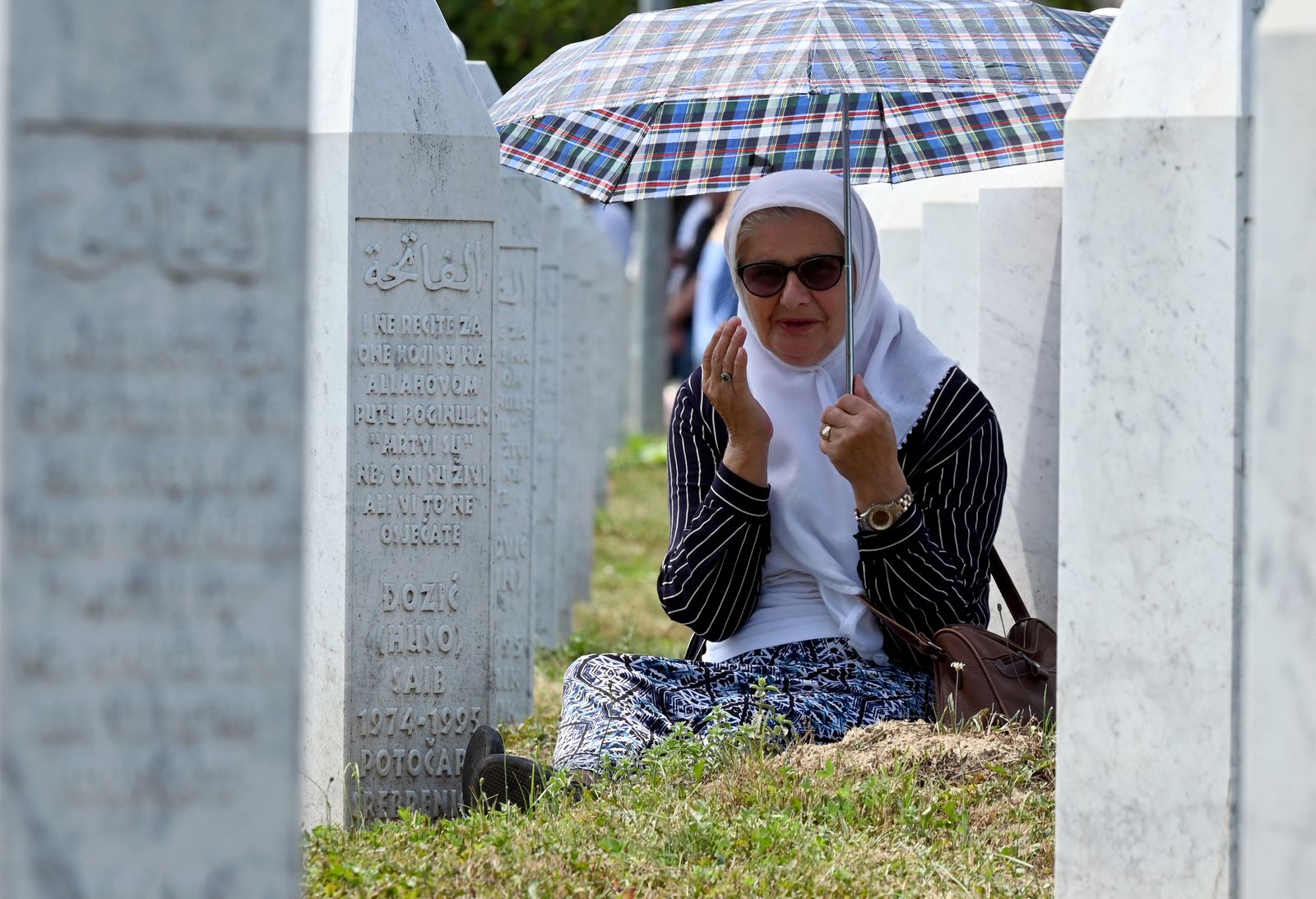 مسلمة بوسنية تحمي نفسها من الشمس بمظلة قبل مراسم دفن التوابيت. 11 يوليو 2021 - AFP
