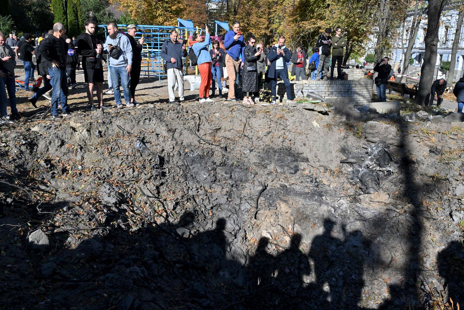 People stand by a rocket crater next to a child playground in central Kyiv on October 10, 2022 after Ukraine's capital was hit by multiple Russian strikes early on today, the first since late June. - The head of the Ukrainian military said that Russian forces launched at least 75 missiles at Ukraine, with fatal strikes targeting the capital Kyiv, and cities in the south and west. (Photo by Sergei SUPINSKY / AFP) - AFP