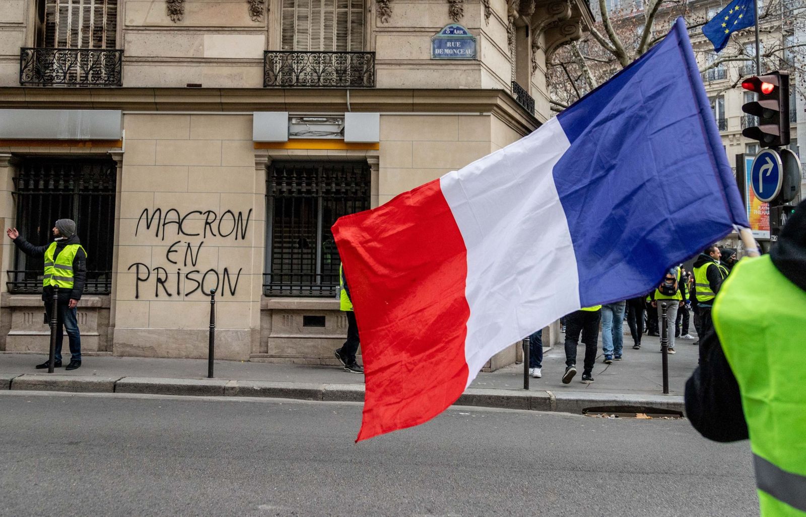 متظاهر يلوّح بعلم فرنسي قرب عبارة على جدار في باريس تطالب بسجن الرئيس الفرنسي إيمانويل ماكرون خلال احتجاجات 