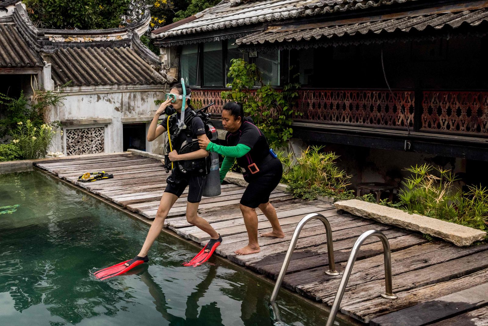 In this photo taken on February 15, 2022, Pijitra Siriaiyara jumps into the swimming pool during a scuba diving lesson at the So Heng Tai mansion in the Talad Noi neighbourhood of Bangkok. - A 200-year-old Chinese mansion in Bangkok's heart isn't an obvious place for a scuba school, but in a city relentlessly demolishing its architectural heritage the business is helping preserve the historic home. (Photo by Jack TAYLOR / AFP) / TO GO WITH Thailand-heritage-architecture-construction, FOCUS by Lisa MARTIN - AFP