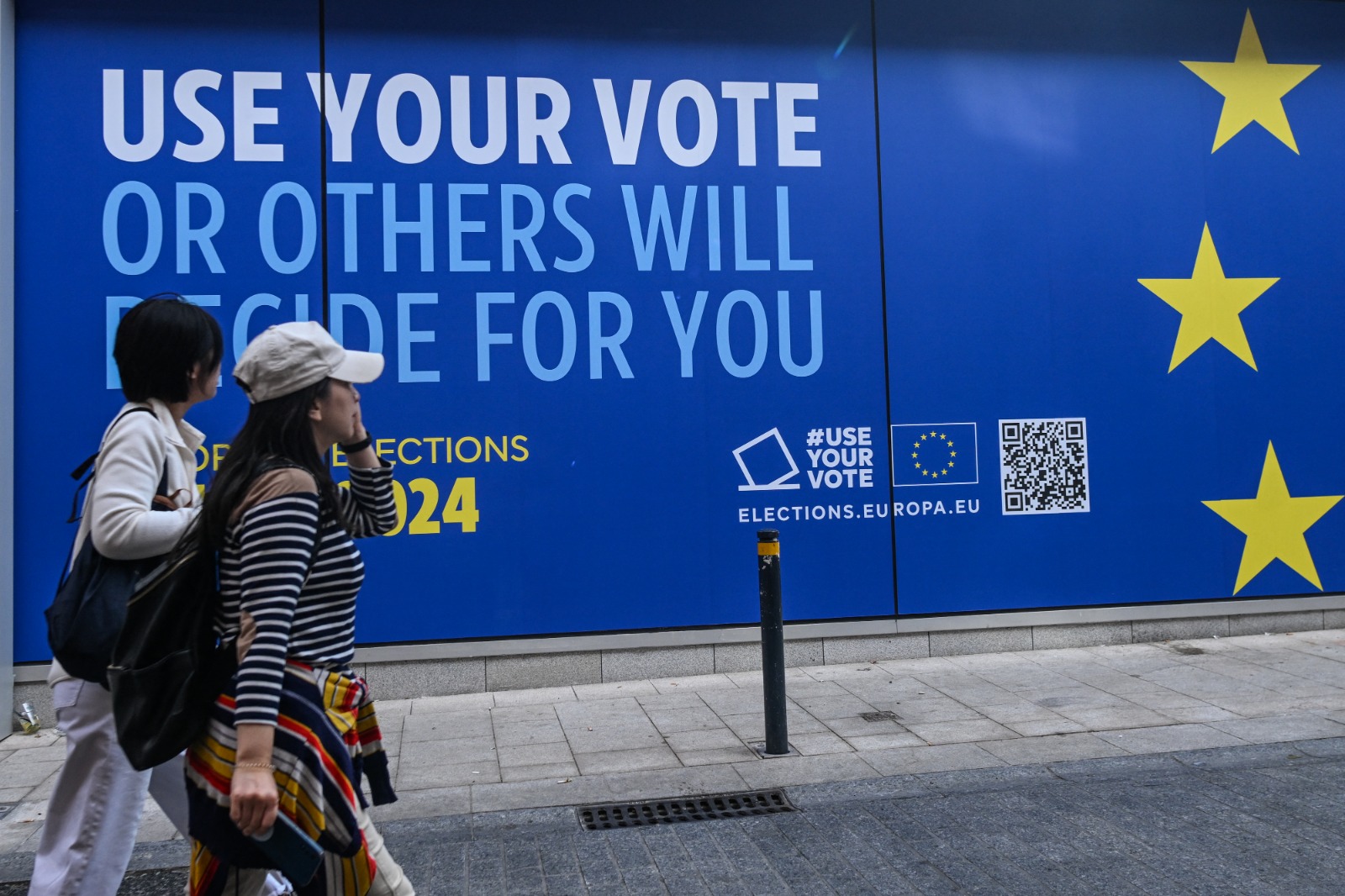 اثنان من المارة يسيران أمام مركز زوار 'تجربة أوروبا' في دبلن، والذي يعلن عن انتخابات البرلمان الأوروبي في 7 يونيو، 21 مايو 2024