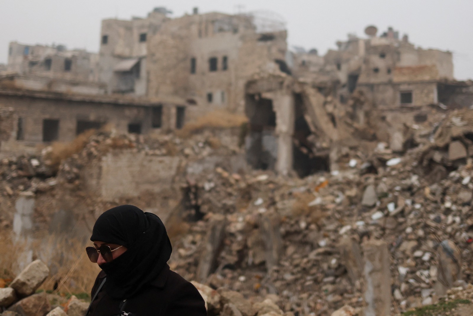 امرأة تسير بجوار مبان مدمرة  في مدينة حلب بعد الإطاحة بنظام بشار الأسد- 22 ديسمبر 2024