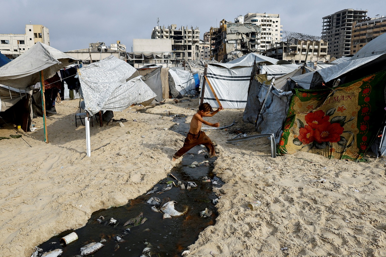 صبي فلسطيني يقفز فوق بركة من مياه الصرف الصحي على الشاطئ وسط حرارة الصيف في مدينة غزة. 12 أغسطس 2025
