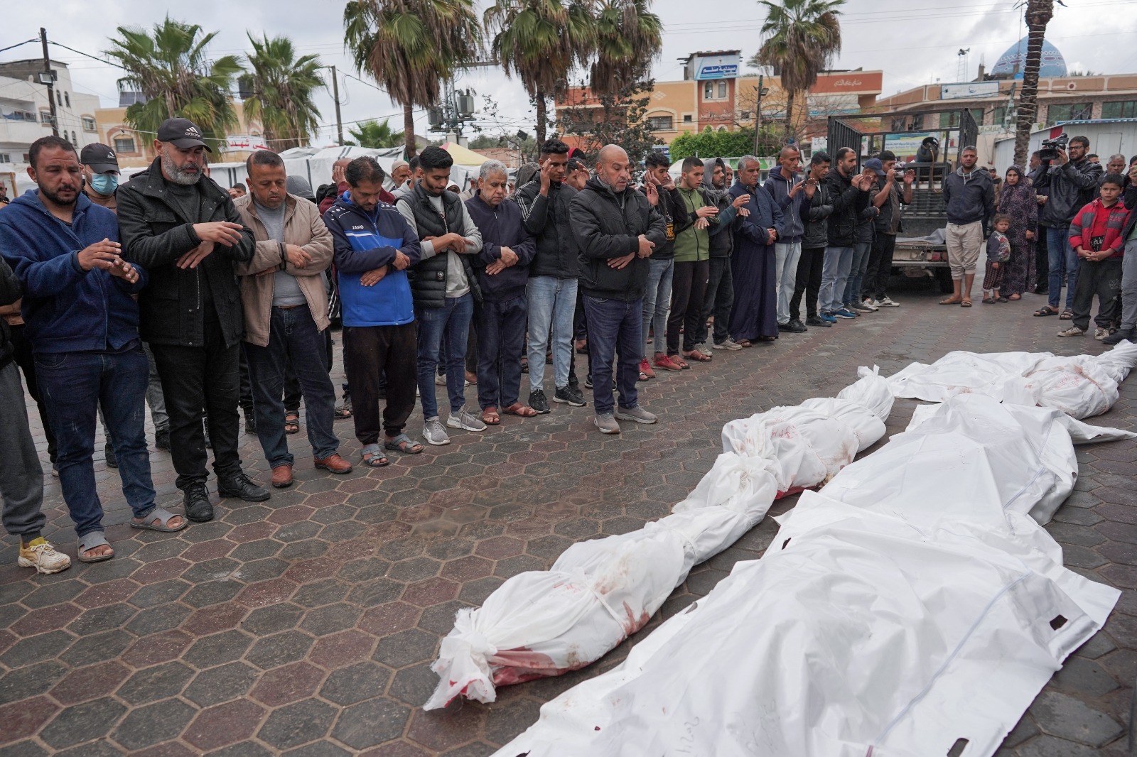 فلسطينيون يصلون صلاة بالقرب من جثامين أفراد عائلة لقيت حتفها جراء القصف الإسرائيلي عشية عيد الفطر على مخيم النصيرات للاجئين في دير البلح. غزة، فلسطين. 10 أبريل 2024