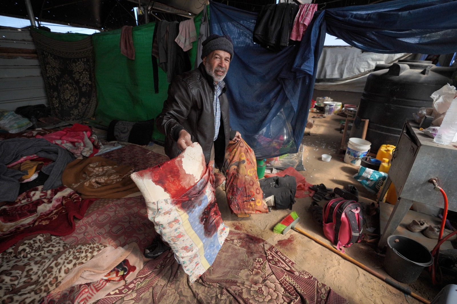 فلسطيني سعى للجوء داخل حظيرة في مخيم المواسي المؤقت للنازحين غرب خان يونس جنوب قطاع غزة يُظهر الوسائد الملطخة بالدماء التي استخدمها أفراد العائلة بعد ضربة إسرائيلية. 11 مارس 2024