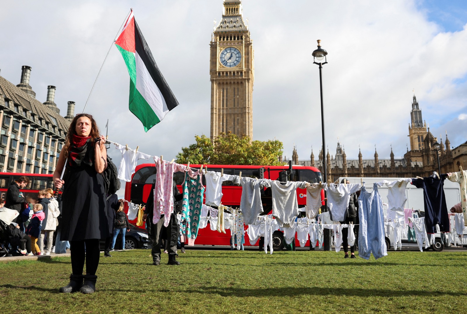 متظاهرة تحمل العلم الفلسطيني بجانب ملابس أطفال خارج مبنى البرلمان في لندن خلال احتجاج لتكريم الأطفال الفلسطينيين الرضع الذين قتلتهم إسرائيل في قطاع غزة - REUTERS